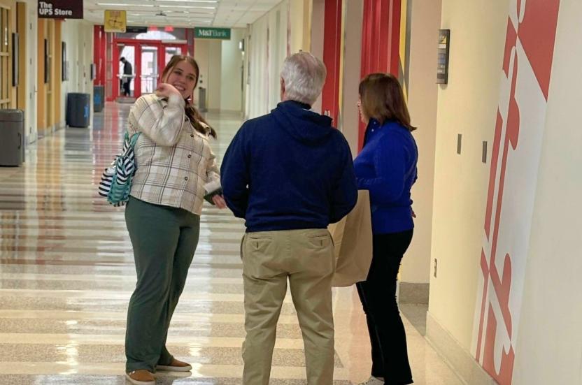 A student standing and talking to two people in a hallway