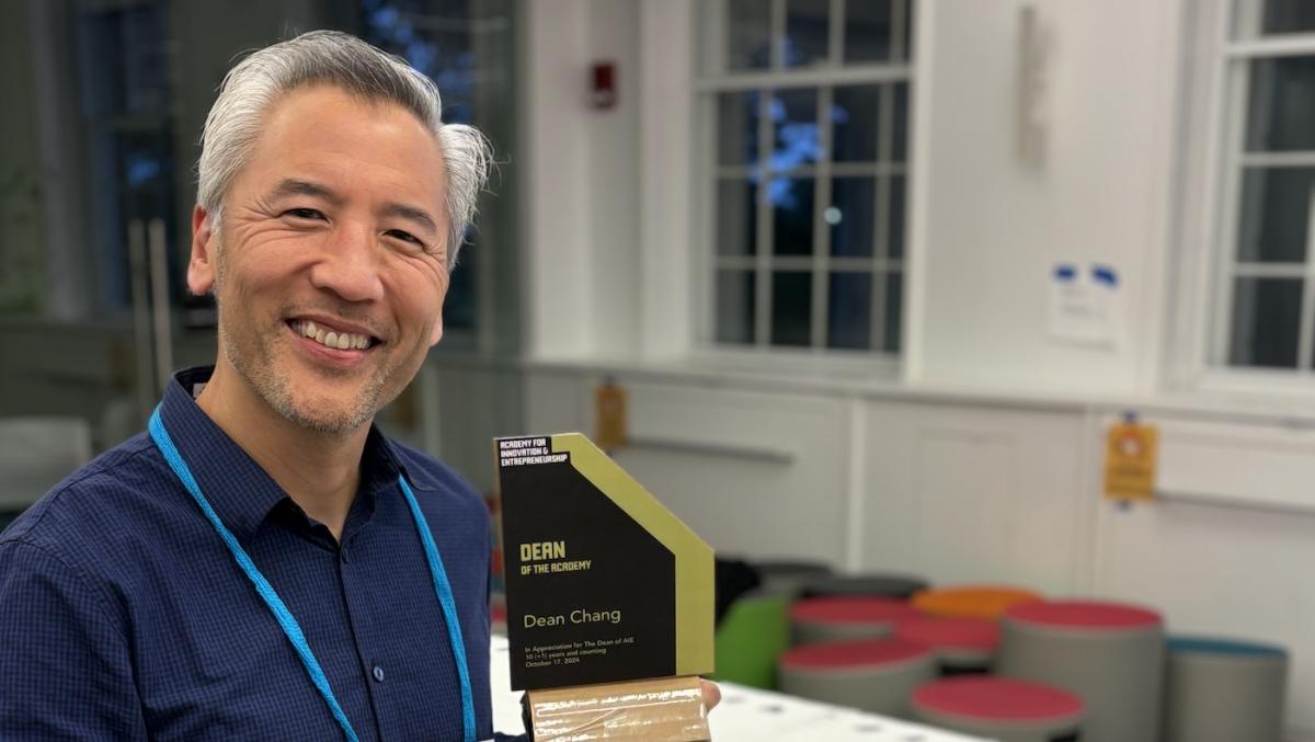 Dean Chang smiling while holding his "Dean of the Academy" award