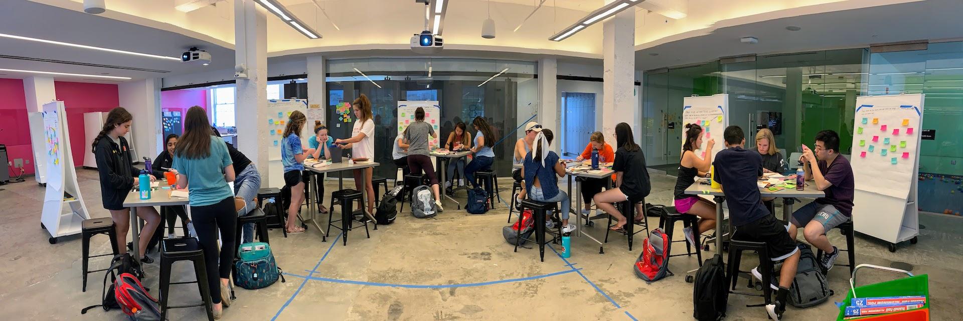 Students working in groups at tables around a classroom