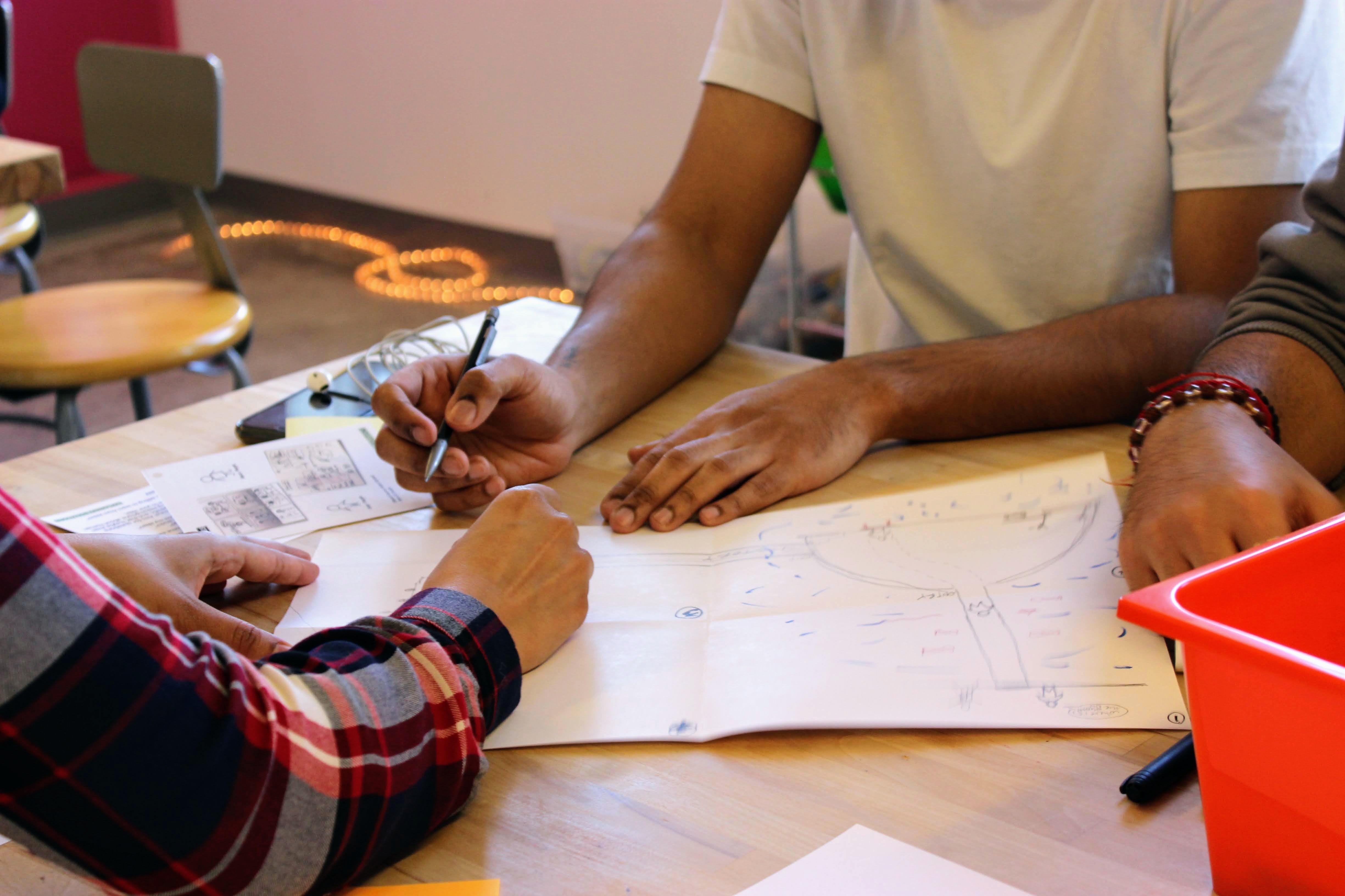 Close up view showing the hands of three different people drawing on a piece of paper together