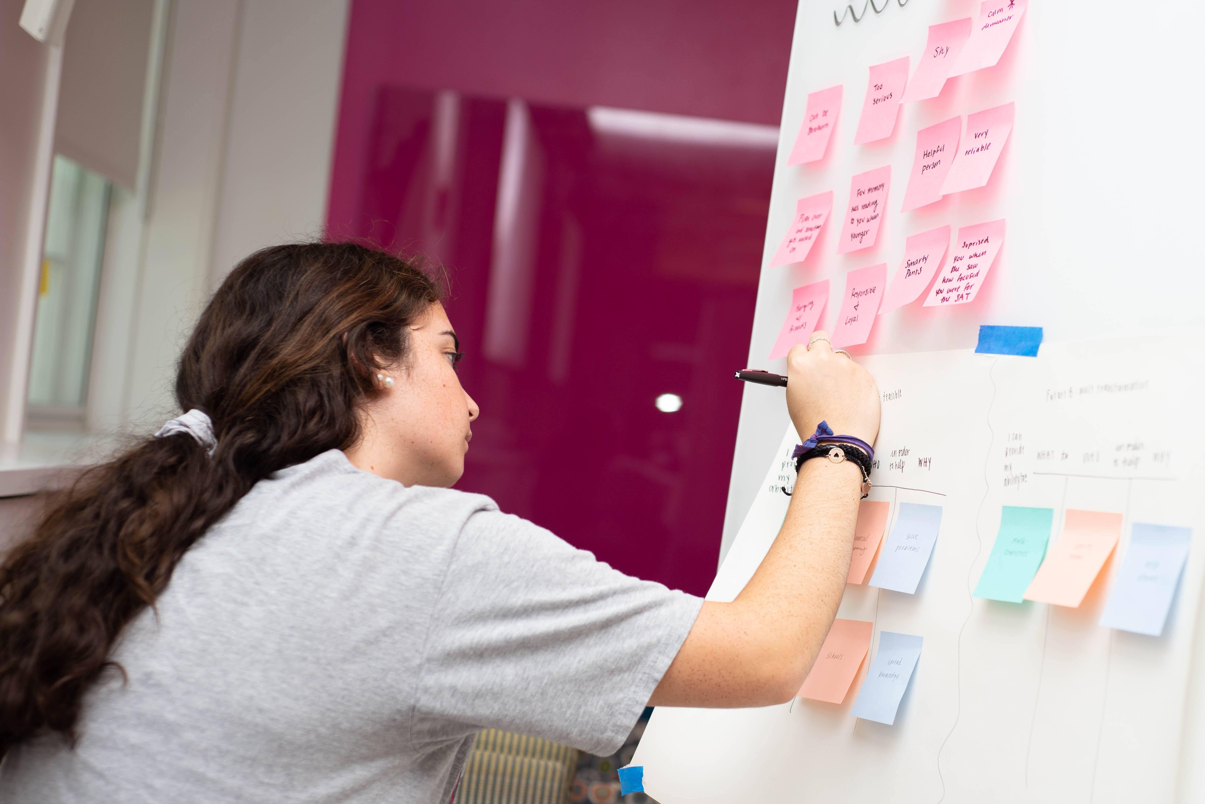 Student working on whiteboard that is covered in post-it notes