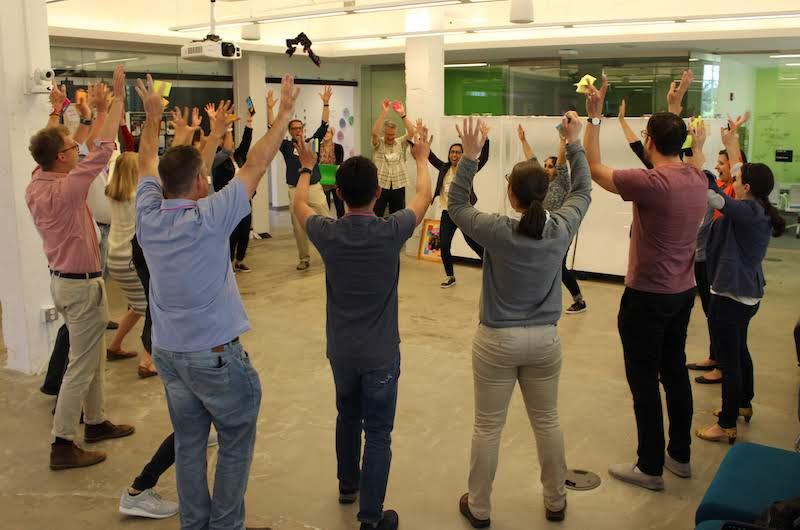 About 20 people standing in a circle with their arms in the air smiling