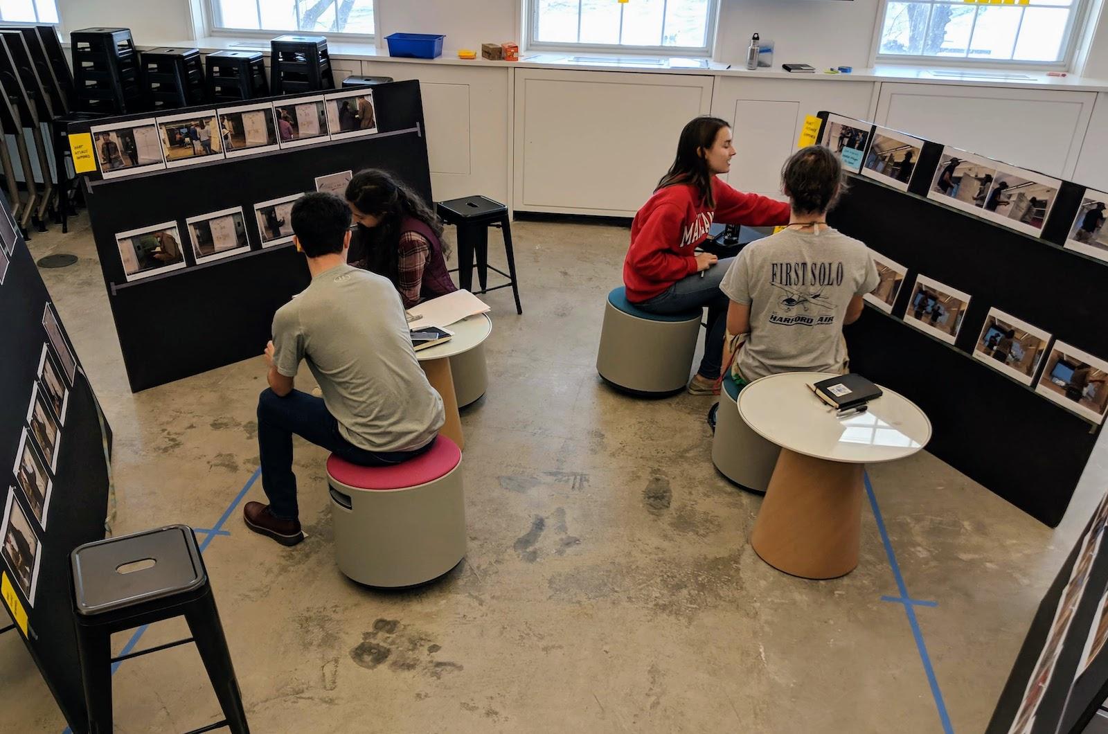 Two groups of students sitting down working in pairs looking at photos on a board