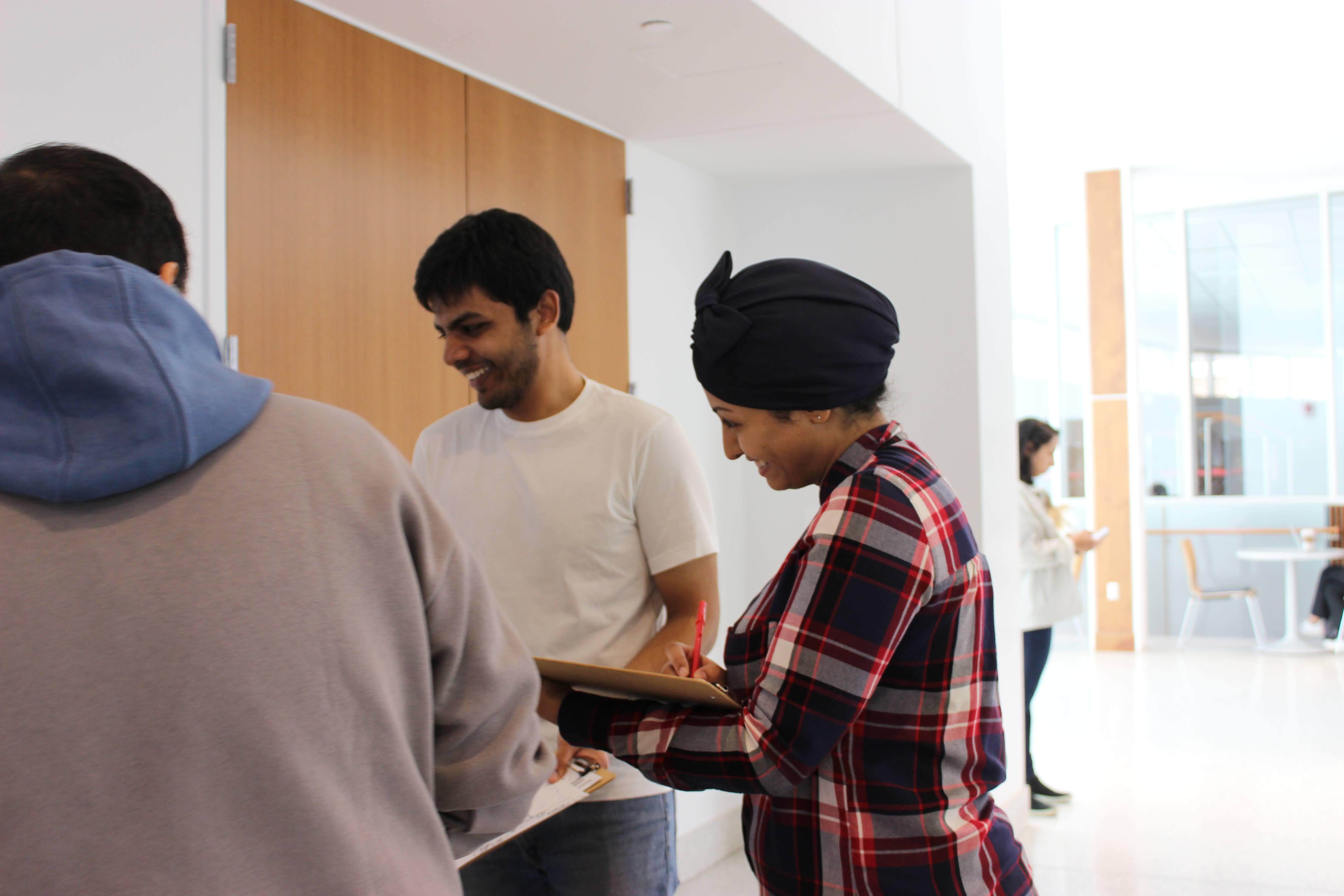 A women smiling while taking notes in a notebook as she stands with two other people